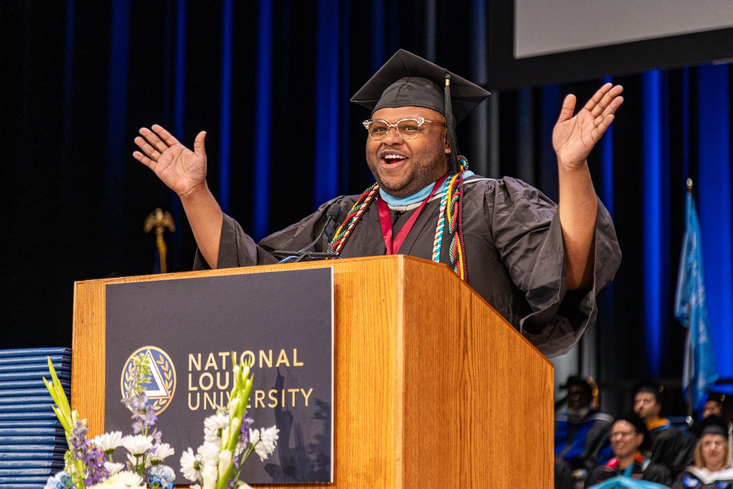 A student in graduation regalia speaking at a podium